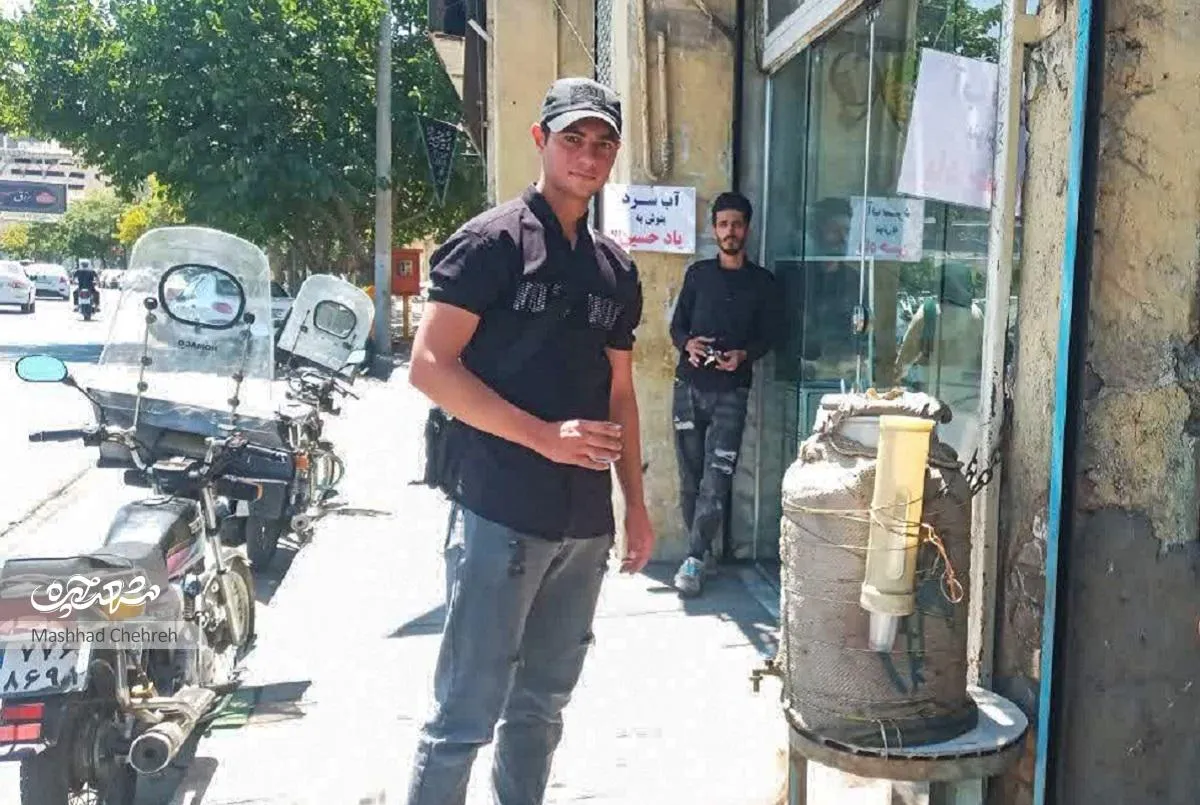 جمشید قدرتی با کلمن جلوی مغازه‌اش، رهگذران را سیراب می‌کند